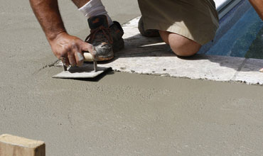 A mason is leveling the cement on the floor